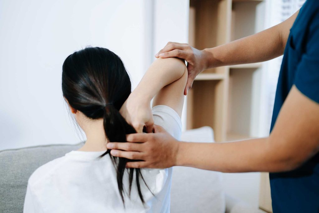 Physical therapist guiding a seated woman through a neck and shoulder stretch in a clinical setting.